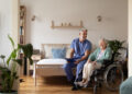 Pflegekraft spricht mit älterer Frau im Rollstuhl in einem wohnlichen Pflegezimmer – Indoor Funkvermessung für stabile Netzversorgung in Pflegeeinrichtungen